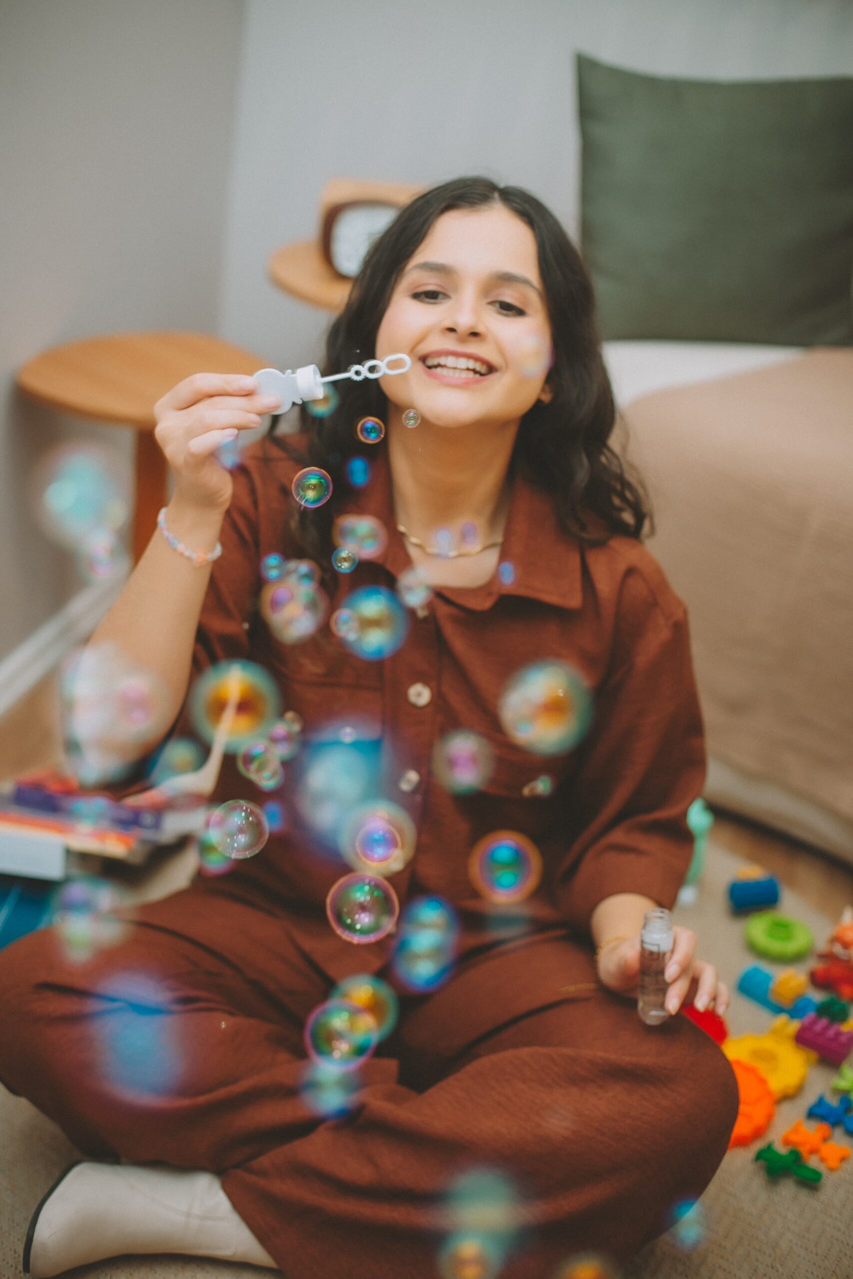 Kananda sentada no chão do consultório soprando bolhas de sabão, cercada de brinquedos coloridos